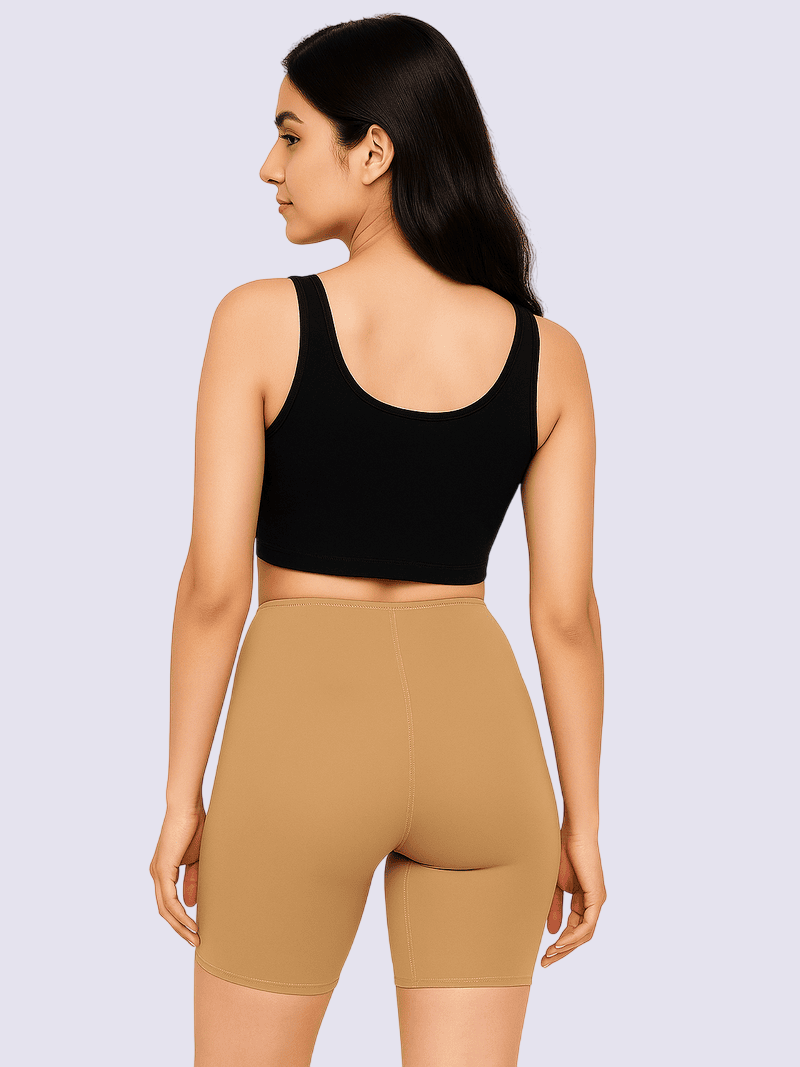 Woman wearing a black sports bra and tan shorts on a light purple background